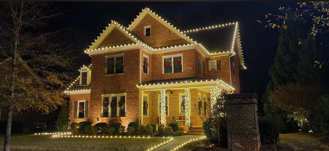 Warm Christmas lights outlining a brick home, porch, and front walkway