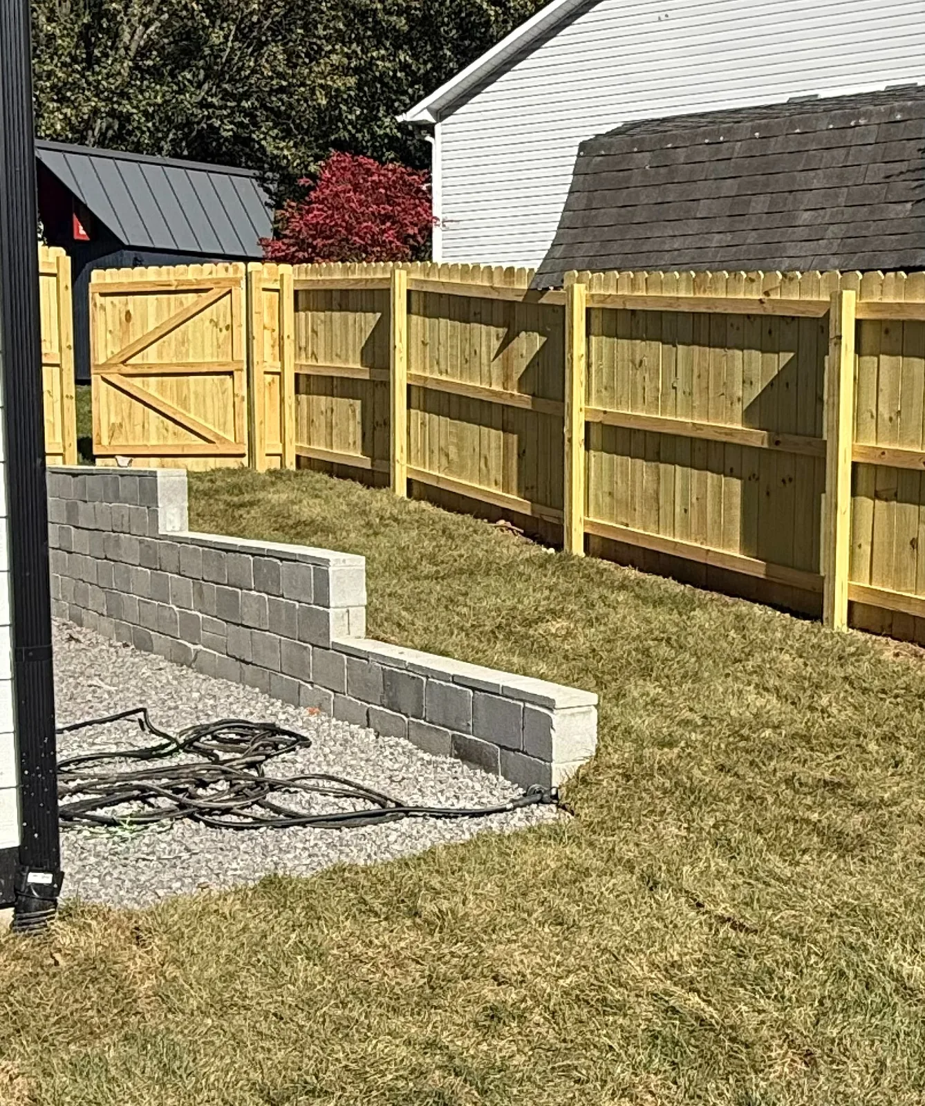 A stepped gray block landscape wall beside a lawn and wooden fence