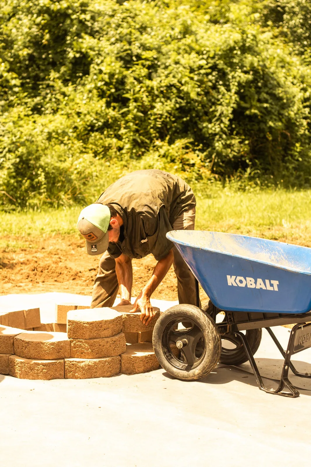 Hands aligning textured landscape blocks around a circular fire pit